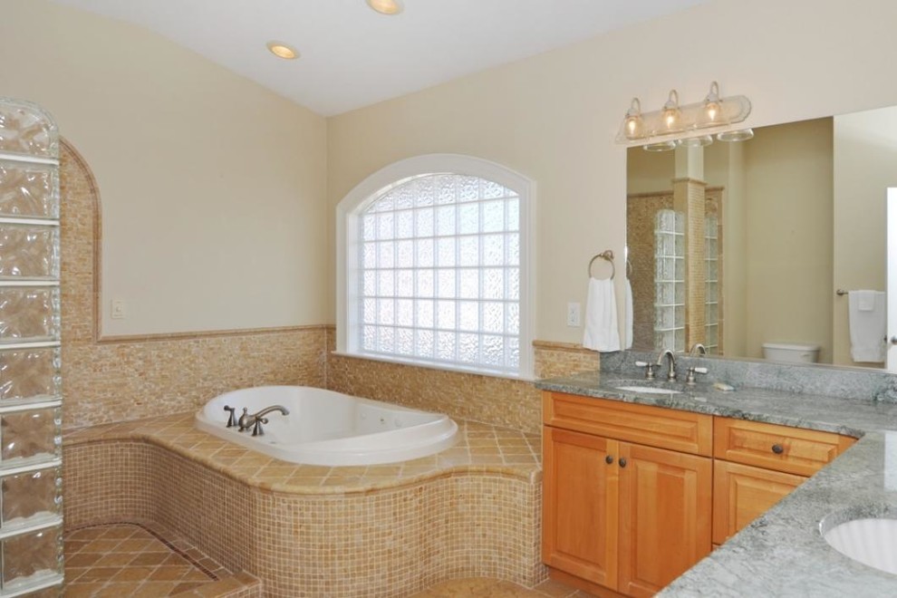 This is an example of a large traditional master wet room bathroom in Other with raised-panel cabinets, medium wood cabinets, a drop-in tub, beige tile, limestone, beige walls, porcelain floors, an undermount sink, granite benchtops, multi-coloured floor and an open shower.