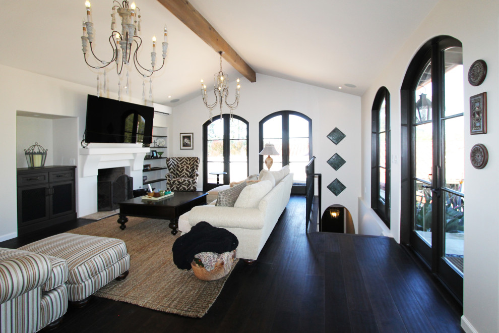 Large tuscan open concept dark wood floor, black floor and vaulted ceiling living room photo in Los Angeles with white walls, a standard fireplace, a plaster fireplace and a wall-mounted tv