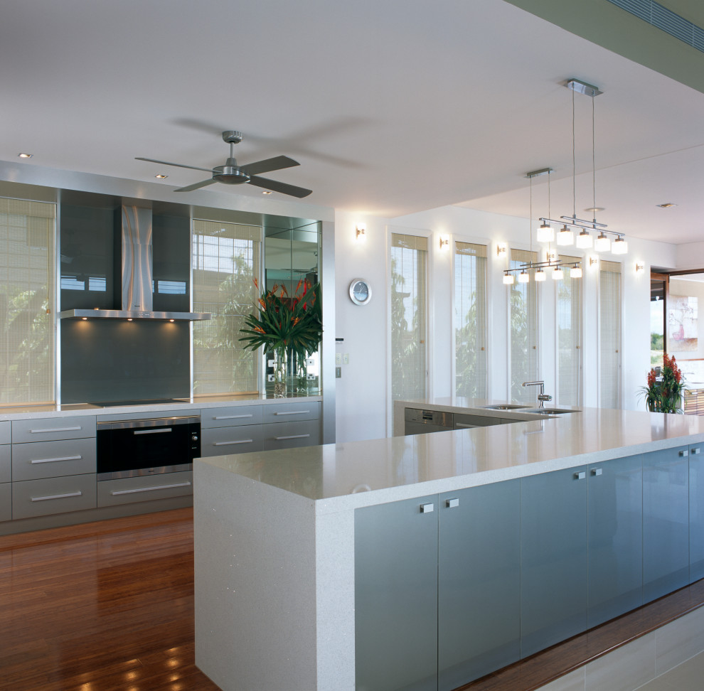 Photo of a modern l-shaped kitchen in Cairns with an undermount sink, grey cabinets, solid surface benchtops, metallic splashback, glass sheet splashback, light hardwood floors, with island and white benchtop.