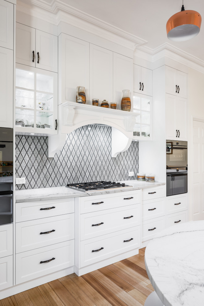 Photo of a traditional galley kitchen in Perth with shaker cabinets, white cabinets, quartzite benchtops, grey splashback, ceramic splashback, stainless steel appliances, light hardwood floors, with island and grey benchtop.