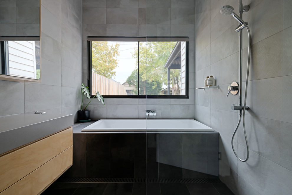 Photo of a contemporary bathroom in Melbourne with flat-panel cabinets, medium wood cabinets, a drop-in tub, a curbless shower, gray tile, grey walls, black floor, an open shower and grey benchtops.