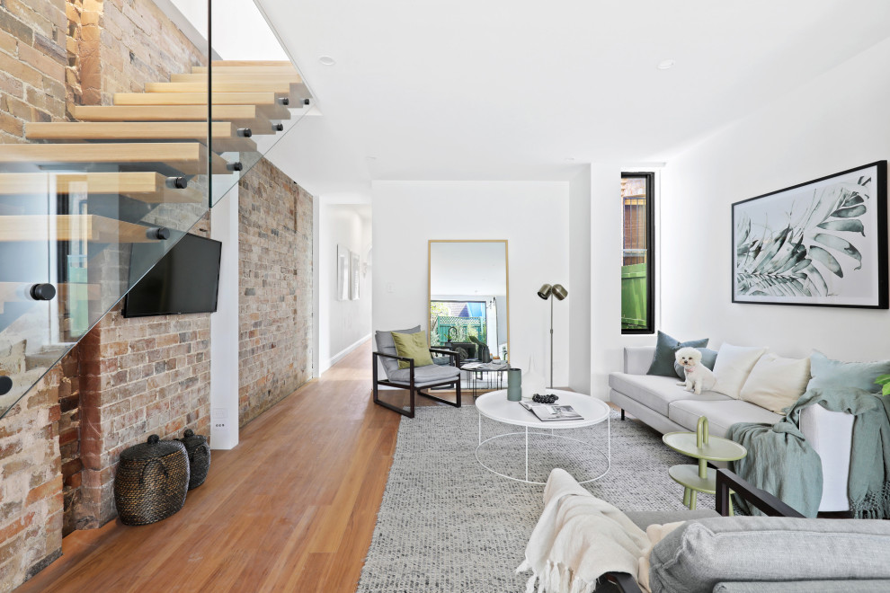 Inspiration for a contemporary open concept living room in Sydney with white walls, medium hardwood floors, no fireplace, a wall-mounted tv, brown floor and brick walls.