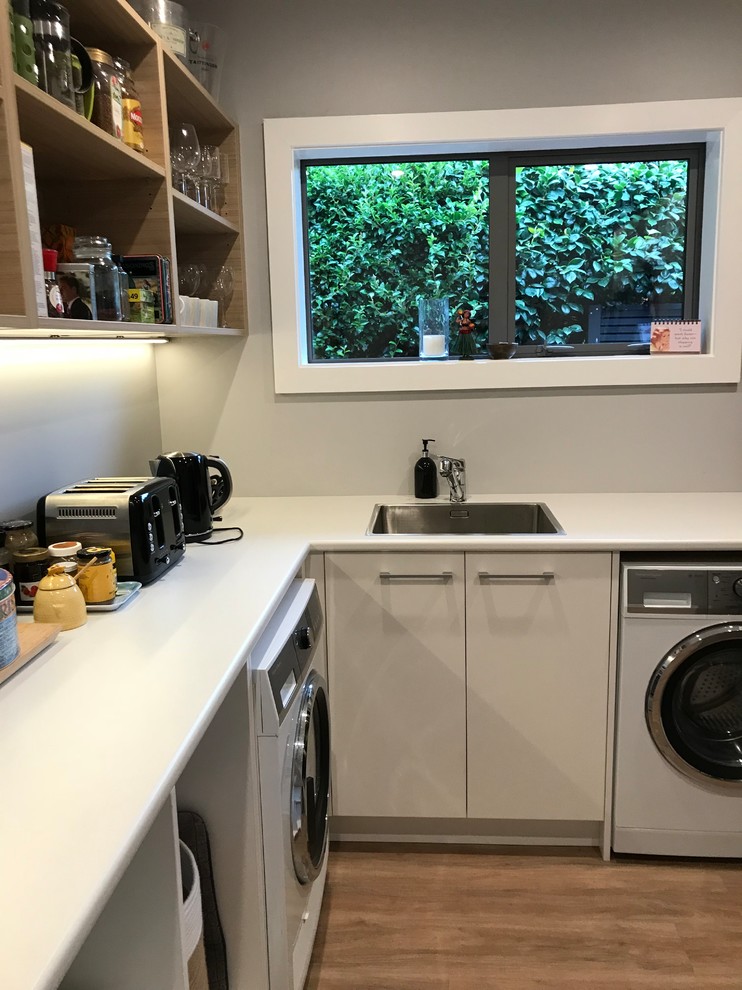 Photo of a large scandinavian galley separate kitchen in Christchurch with a single-bowl sink, flat-panel cabinets, white cabinets, laminate benchtops, stainless steel appliances, vinyl floors and brown floor.