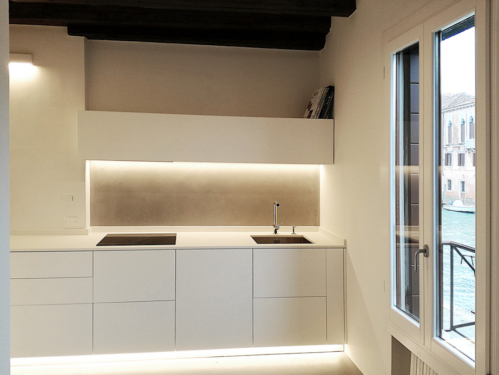 Photo of a small contemporary l-shaped separate kitchen in Venice with a single-bowl sink, flat-panel cabinets, white cabinets, solid surface benchtops, grey splashback, black appliances, concrete floors, no island, grey floor, white benchtop and exposed beam.