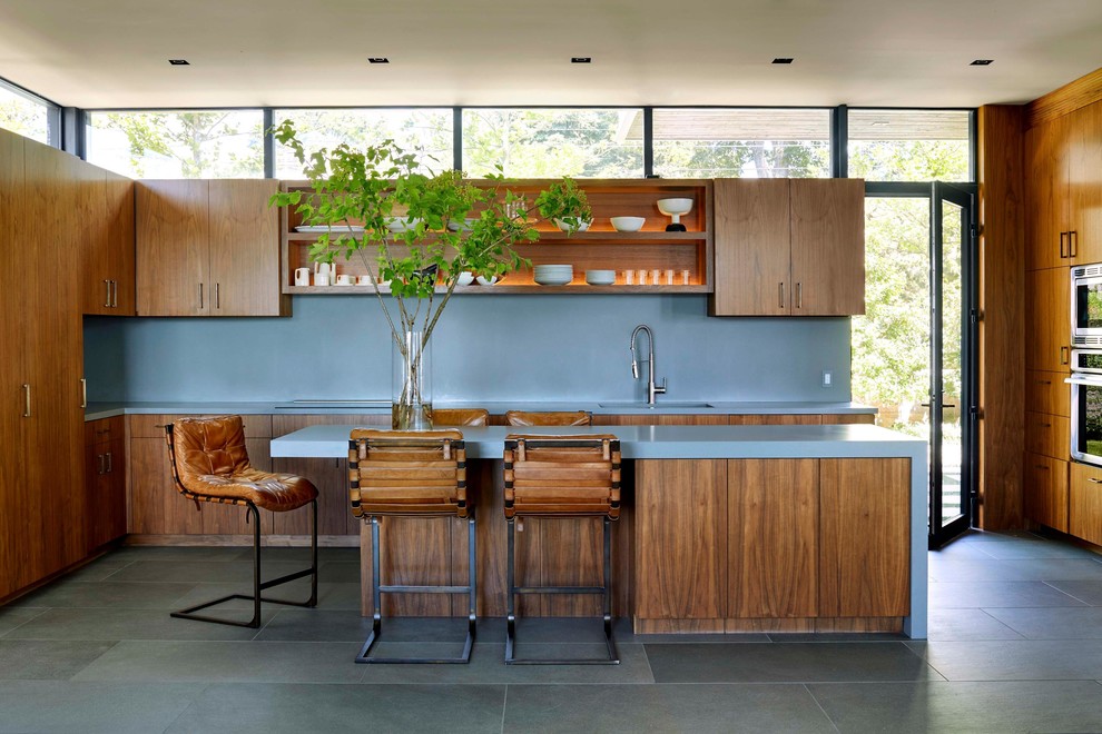 This is an example of a midcentury l-shaped kitchen in New York with a double-bowl sink, flat-panel cabinets, medium wood cabinets, grey splashback, stainless steel appliances, with island, grey floor and grey benchtop.