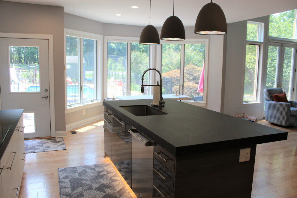 Photo of a mid-sized contemporary l-shaped open plan kitchen in DC Metro with an undermount sink, flat-panel cabinets, grey splashback, ceramic splashback, stainless steel appliances, light hardwood floors, with island and black benchtop.