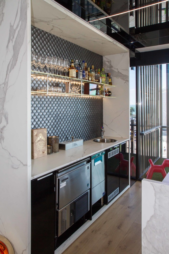 Design ideas for a large modern galley seated home bar in Melbourne with flat-panel cabinets, a drop-in sink, black cabinets, tile benchtops, grey splashback, mosaic tile splashback, medium hardwood floors, brown floor and white benchtop.