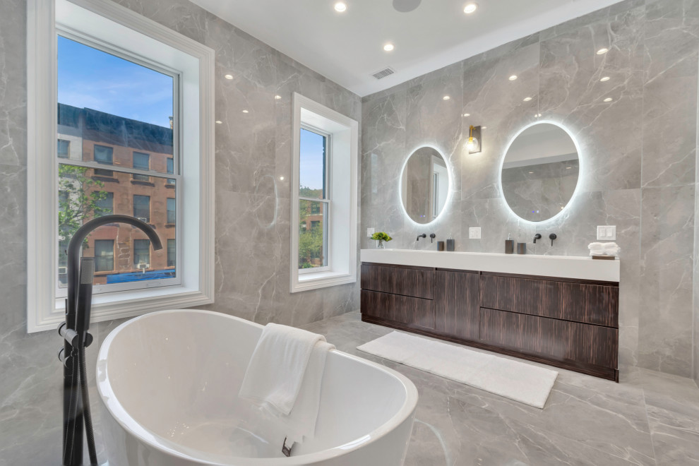 Пример оригинального дизайна: огромная главная ванная комната в современном стиле с плоскими фасадами, искусственно-состаренными фасадами, отдельно стоящей ванной, душевой комнатой, инсталляцией, серой плиткой, керамогранитной плиткой, серыми стенами, полом из керамогранита, накладной раковиной, столешницей из искусственного кварца, серым полом, душем с распашными дверями, белой столешницей, тумбой под две раковины и встроенной тумбой