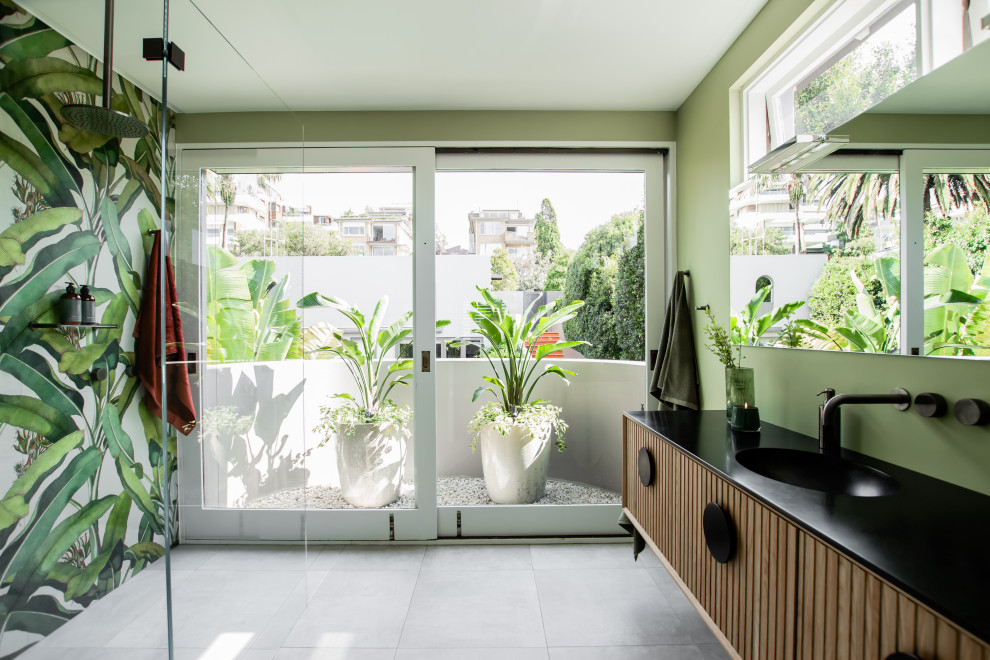 This is an example of a mid-sized contemporary 3/4 bathroom in Sydney with medium wood cabinets, an open shower, a two-piece toilet, green walls, an integrated sink, grey floor, an open shower, black benchtops, a single vanity and a floating vanity.