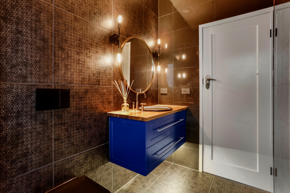 Photo of a mid-sized contemporary powder room in Melbourne with shaker cabinets, blue cabinets, a one-piece toilet, black tile, porcelain tile, black walls, porcelain floors, a drop-in sink, wood benchtops, black floor, brown benchtops and a floating vanity.