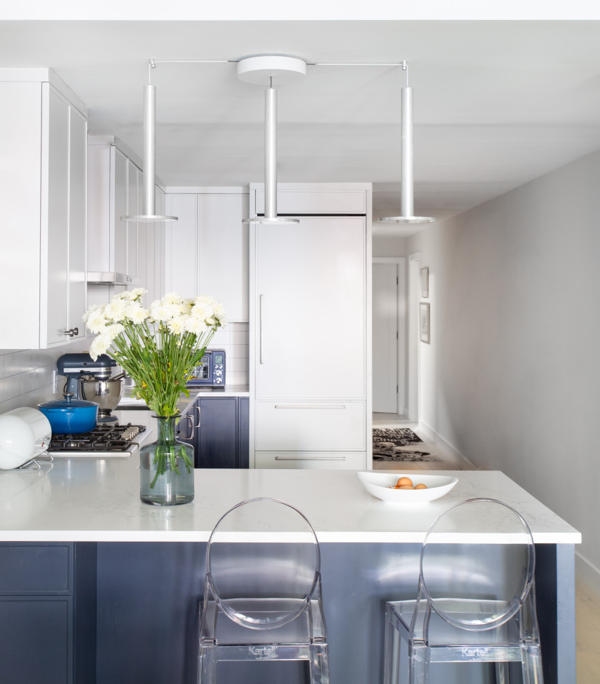 Inspiration for a small modern u-shaped kitchen in New York with a drop-in sink, shaker cabinets, white cabinets, solid surface benchtops, white splashback, ceramic splashback, panelled appliances, medium hardwood floors, with island, white floor and white benchtop.