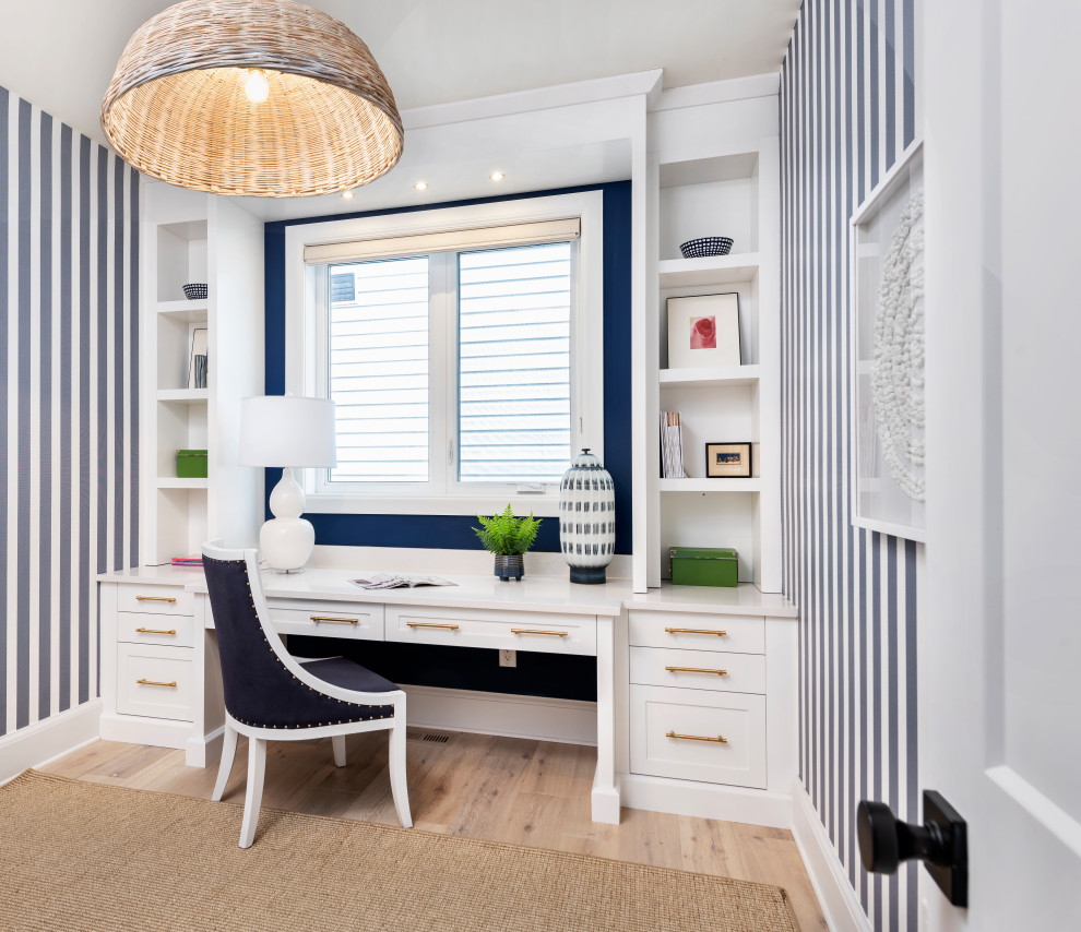 This is an example of a transitional home office in Ottawa with multi-coloured walls, light hardwood floors, a built-in desk, beige floor and wallpaper.