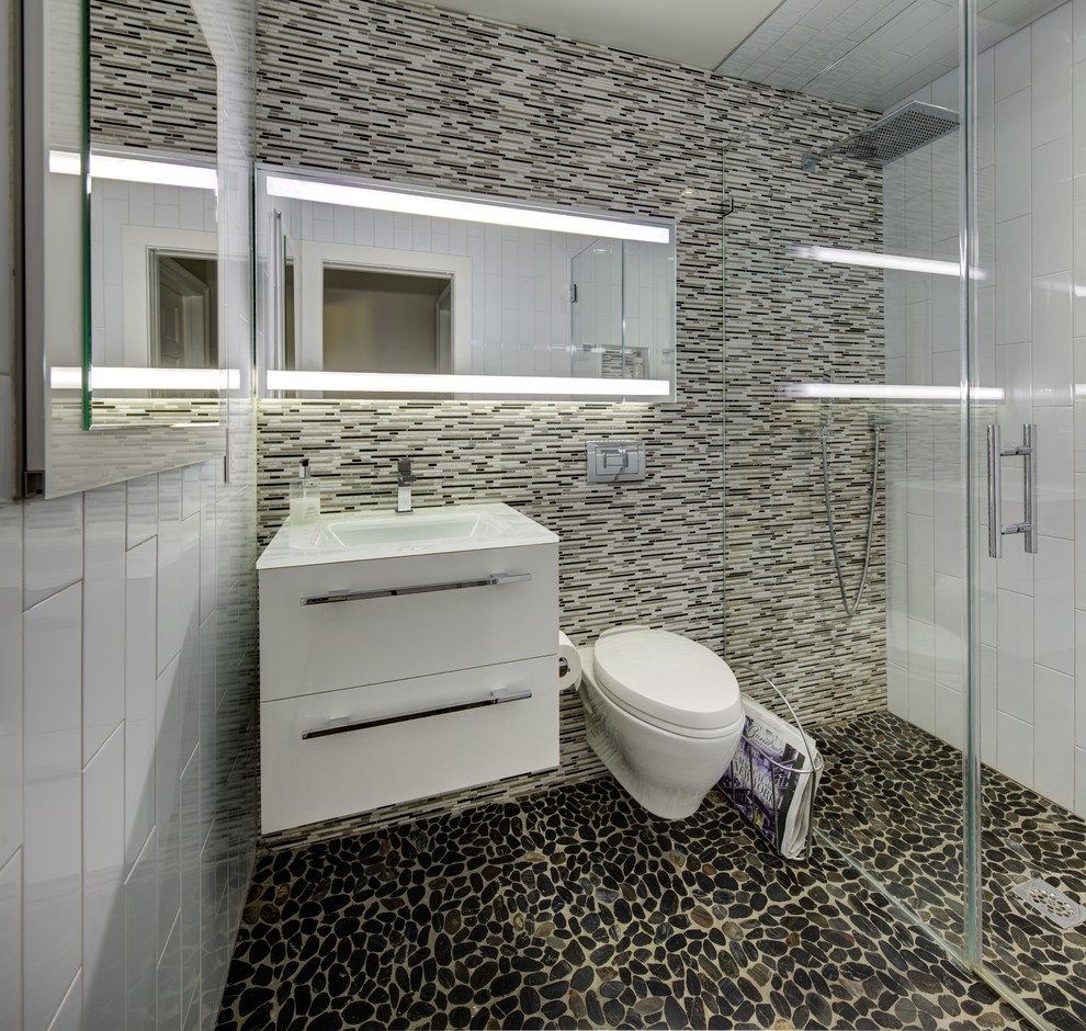 Photo of a small modern master bathroom in New York with flat-panel cabinets, white cabinets, a curbless shower, a wall-mount toilet, black and white tile, matchstick tile, white walls, pebble tile floors, glass benchtops and an integrated sink.