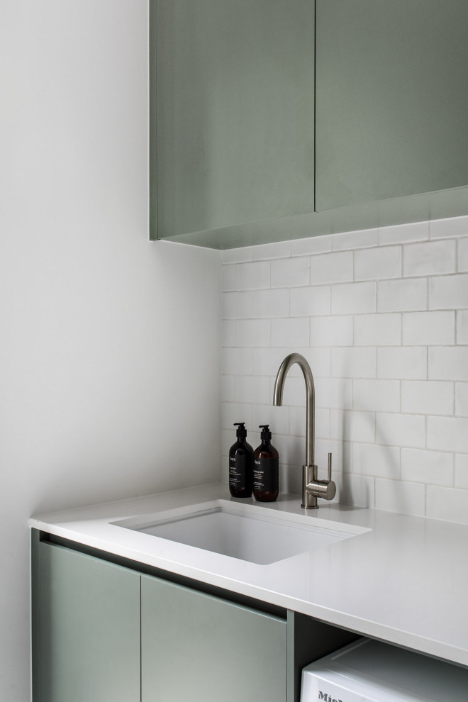 Design ideas for a medium sized contemporary galley separated utility room in Melbourne with a built-in sink, flat-panel cabinets, green cabinets, limestone worktops, white splashback, metro tiled splashback, white walls, porcelain flooring, an integrated washer and dryer, grey floors and white worktops.
