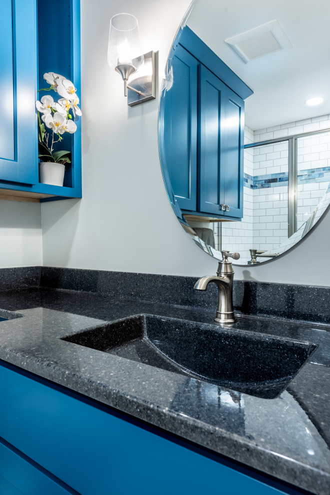 Photo of a small transitional 3/4 bathroom in Other with blue cabinets, an alcove shower, a two-piece toilet, white tile, subway tile, grey walls, vinyl floors, an integrated sink, onyx benchtops, white floor, a sliding shower screen, grey benchtops, a single vanity and a built-in vanity.