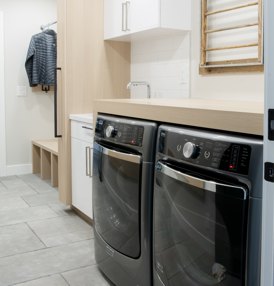 This is an example of a mid-sized modern single-wall utility room in San Francisco with an undermount sink, flat-panel cabinets, light wood cabinets, wood benchtops, grey walls, limestone floors, a side-by-side washer and dryer, grey floor and brown benchtop.