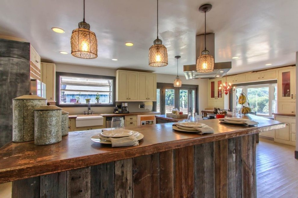 Mid-sized mountain style u-shaped light wood floor eat-in kitchen photo with a farmhouse sink, raised-panel cabinets, beige cabinets, wood countertops, stainless steel appliances and an island