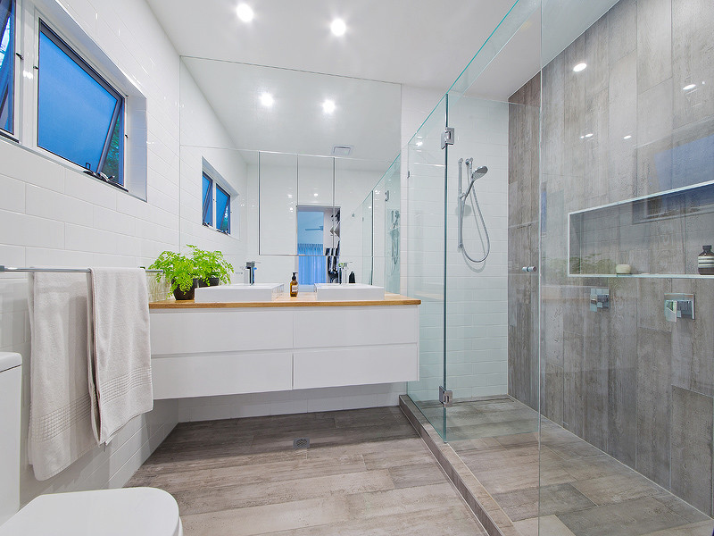 Photo of a mid-sized modern bathroom in Brisbane with beaded inset cabinets, white cabinets, an alcove shower, a wall-mount toilet, gray tile, cement tile, white walls, cement tiles, a vessel sink, wood benchtops, grey floor, a hinged shower door and brown benchtops.
