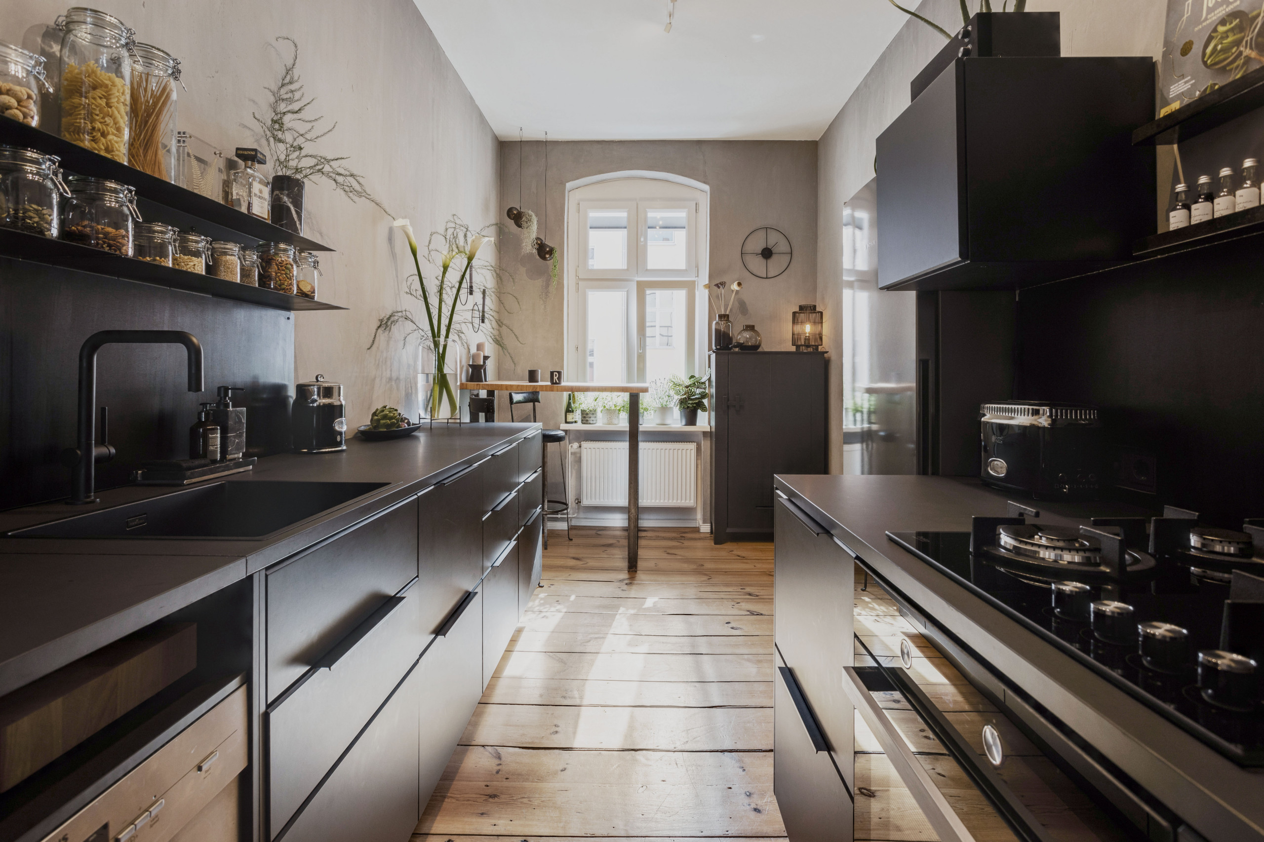 Trendy galley medium tone wood floor and brown floor kitchen photo in Berlin with an integrated sink, flat-panel cabinets, black cabinets, black backsplash, black appliances and black countertops