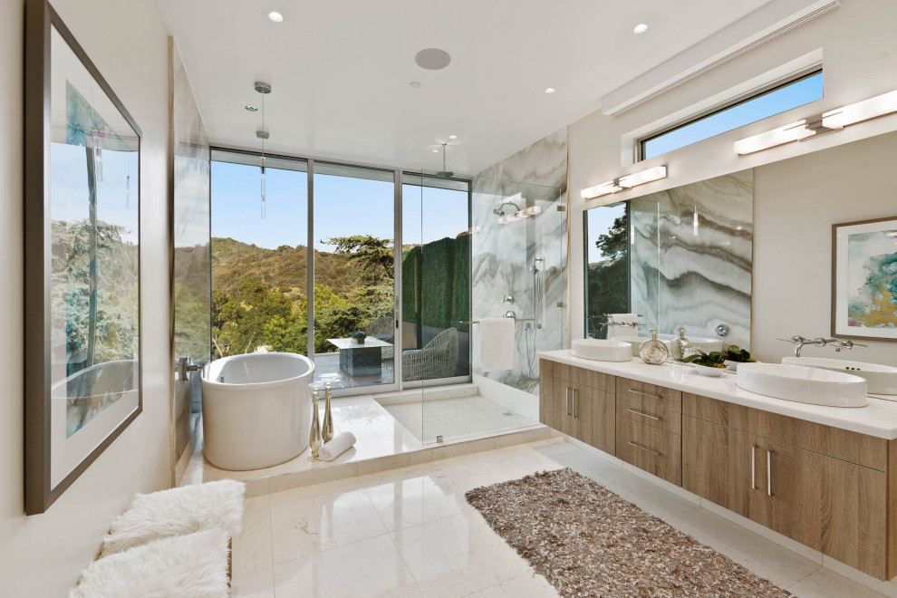 Inspiration for a large contemporary master wet room bathroom in Los Angeles with flat-panel cabinets, a freestanding tub, stone slab, beige walls, porcelain floors, a vessel sink, solid surface benchtops, an open shower, white benchtops, beige floor, medium wood cabinets, multi-coloured tile, a double vanity and a floating vanity.
