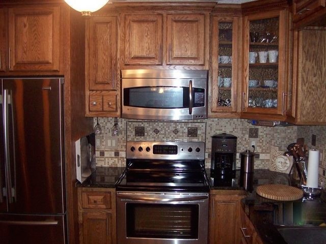 Large galley light wood floor enclosed kitchen photo in Cedar Rapids with a drop-in sink, raised-panel cabinets, medium tone wood cabinets, multicolored backsplash, stainless steel appliances and an island