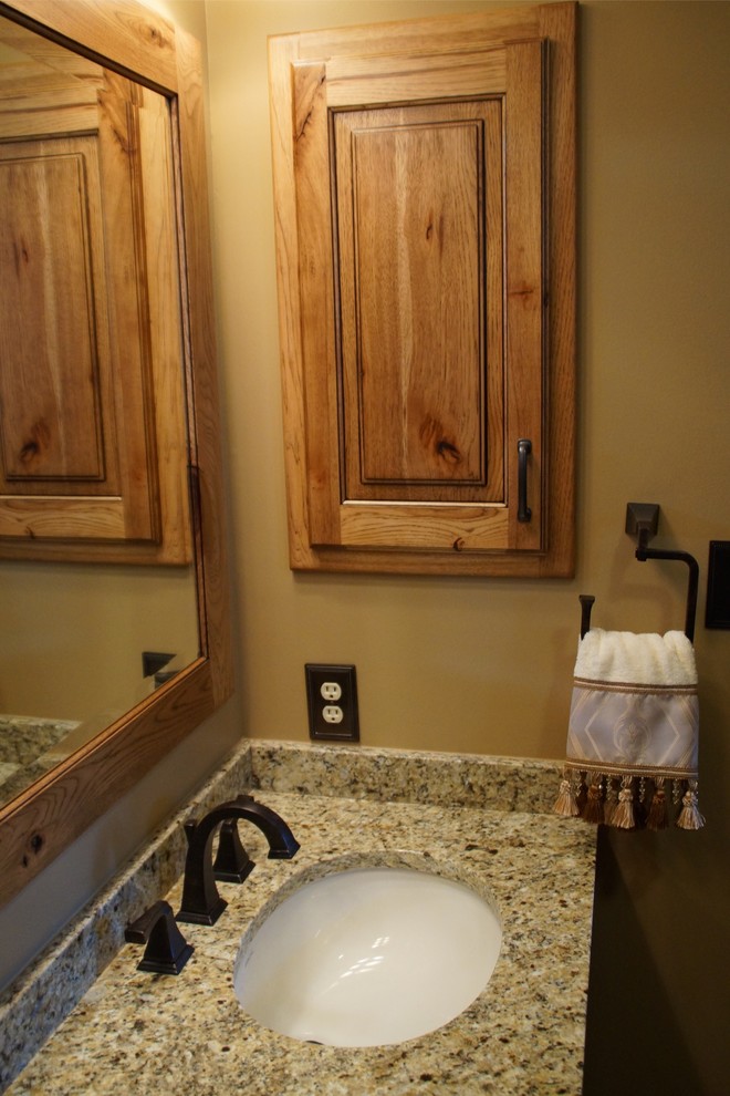 Example of a mid-sized mountain style master multicolored tile and stone tile travertine floor alcove shower design with raised-panel cabinets, medium tone wood cabinets, a one-piece toilet, beige walls, an undermount sink and granite countertops