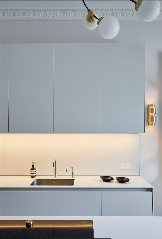 Large contemporary single-wall eat-in kitchen in London with a single-bowl sink, flat-panel cabinets, solid surface benchtops, white splashback, medium hardwood floors, with island, grey floor and coffered.