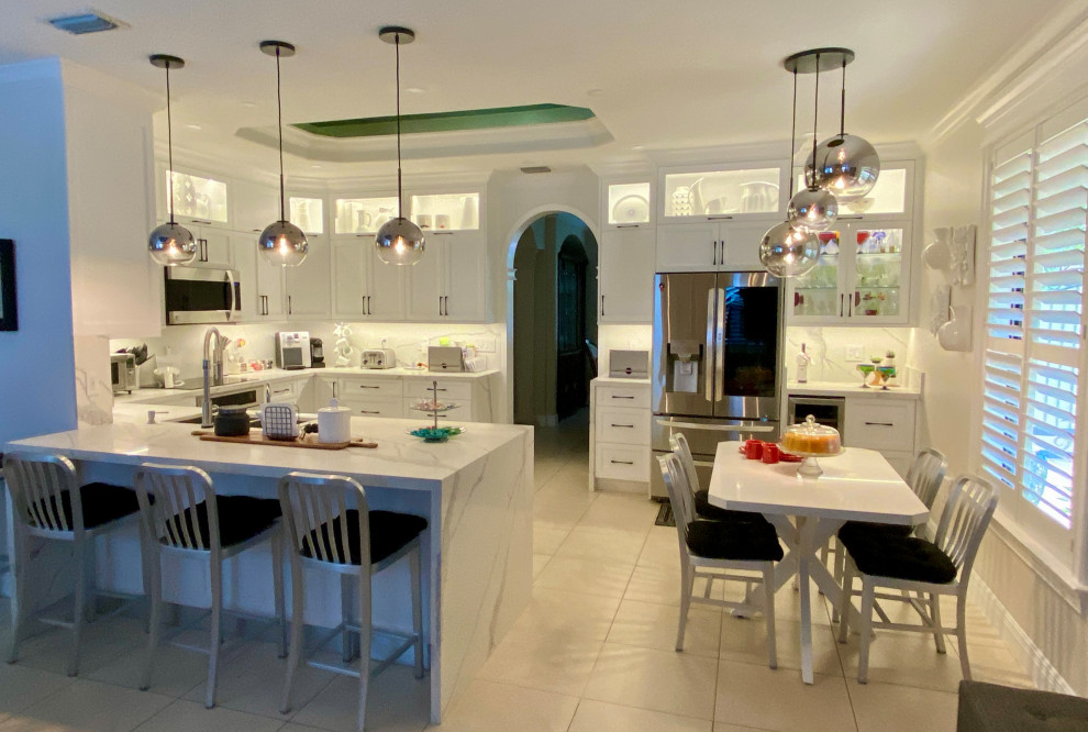 Transitional u-shaped porcelain tile, beige floor and coffered ceiling open concept kitchen photo in Miami with a double-bowl sink, shaker cabinets, white cabinets, quartz countertops, white backsplash, quartz backsplash, stainless steel appliances, a peninsula and white countertops