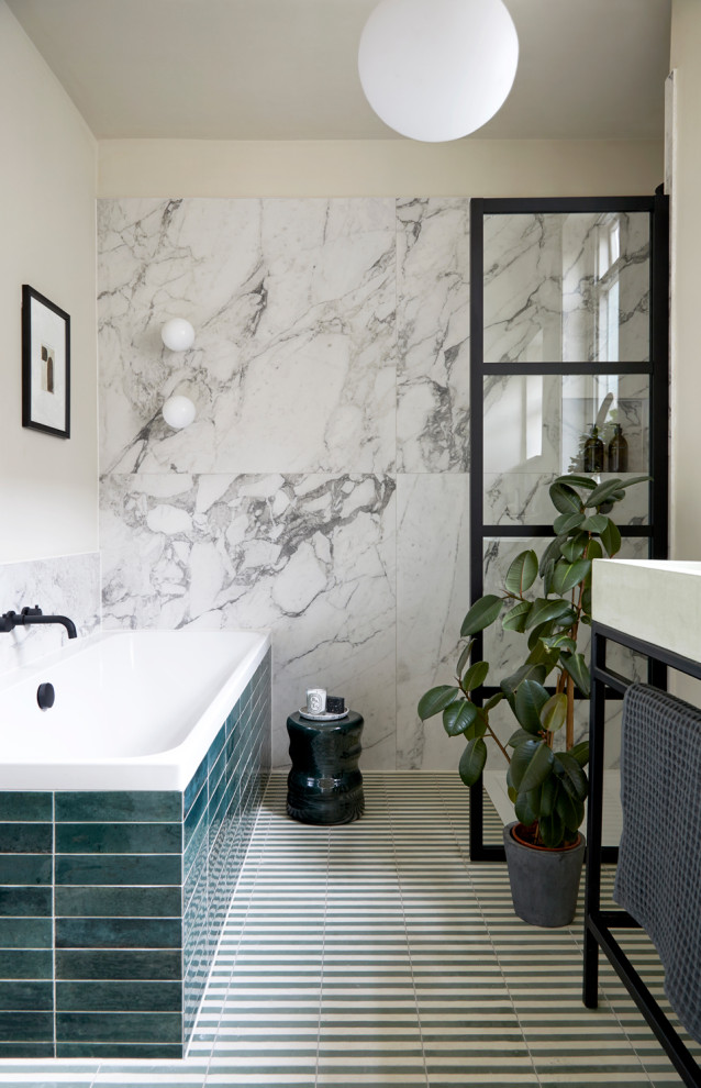 This is an example of a mid-sized modern kids bathroom in London with a drop-in tub, an open shower, a wall-mount toilet, black and white tile, marble, cement tiles, a pedestal sink, green floor, an open shower, a single vanity and a freestanding vanity.