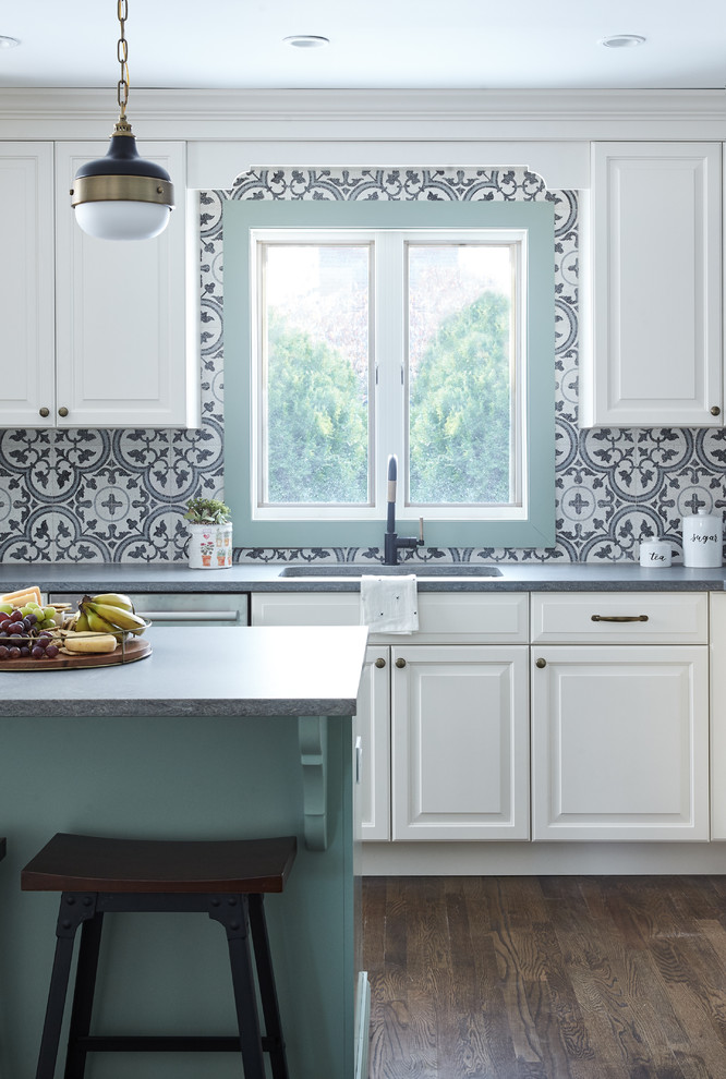 Inspiration for a mid-sized country l-shaped eat-in kitchen in New York with an undermount sink, raised-panel cabinets, white cabinets, quartz benchtops, multi-coloured splashback, cement tile splashback, stainless steel appliances, medium hardwood floors, brown floor and grey benchtop.