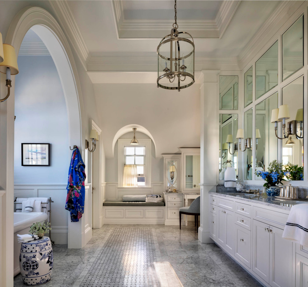На фото: большая главная, серо-белая ванная комната в классическом стиле с белыми фасадами, отдельно стоящей ванной, белыми стенами, мраморным полом, серым полом, тумбой под две раковины, встроенной тумбой и многоуровневым потолком