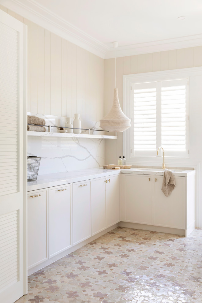 Example of a large mountain style ceramic tile, multicolored floor and wall paneling laundry room design in Sydney with beige cabinets, marble countertops, white backsplash, marble backsplash, beige walls, a side-by-side washer/dryer and white countertops