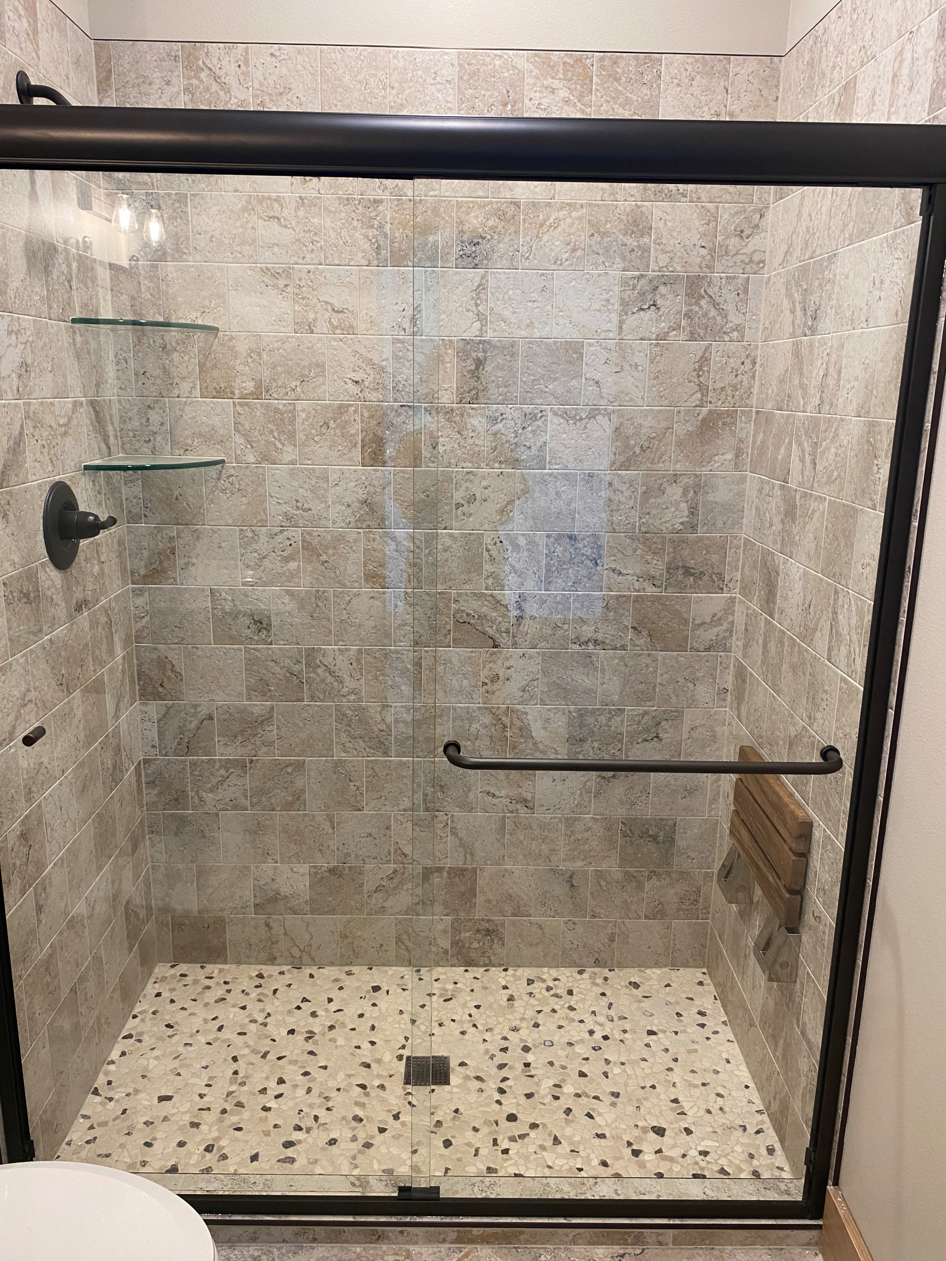 Custom tile shower with foldable teak bench, glass shower shelves, and glass sho