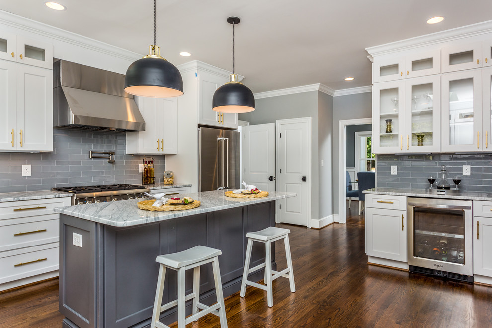 Design ideas for a traditional kitchen in Raleigh with glass-front cabinets, white cabinets, grey splashback, subway tile splashback, stainless steel appliances, dark hardwood floors, with island and brown floor.