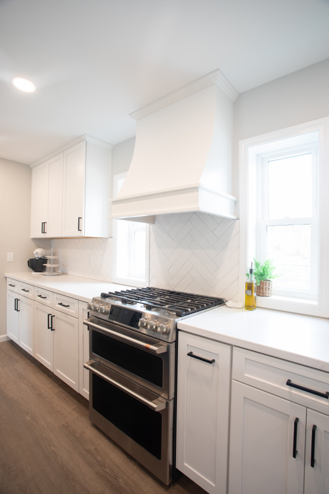 Transitional vinyl floor kitchen photo with shaker cabinets, white cabinets, quartz countertops, white backsplash, porcelain backsplash, stainless steel appliances and white countertops