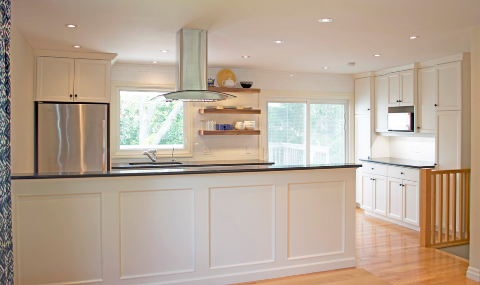 Open concept kitchen - mid-sized transitional galley light wood floor open concept kitchen idea with an undermount sink, shaker cabinets, white cabinets, quartzite countertops, white backsplash, subway tile backsplash, stainless steel appliances, a peninsula and black countertops