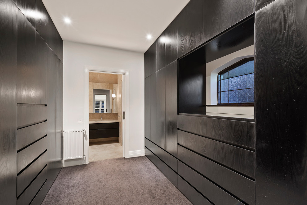 Photo of a large contemporary gender-neutral walk-in wardrobe in Melbourne with flat-panel cabinets, dark wood cabinets and carpet.