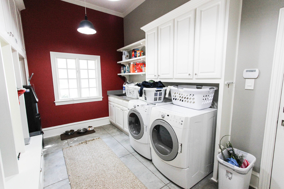 This is an example of a large transitional single-wall dedicated laundry room with white cabinets, a side-by-side washer and dryer, an undermount sink, raised-panel cabinets, laminate benchtops, red walls and ceramic floors.