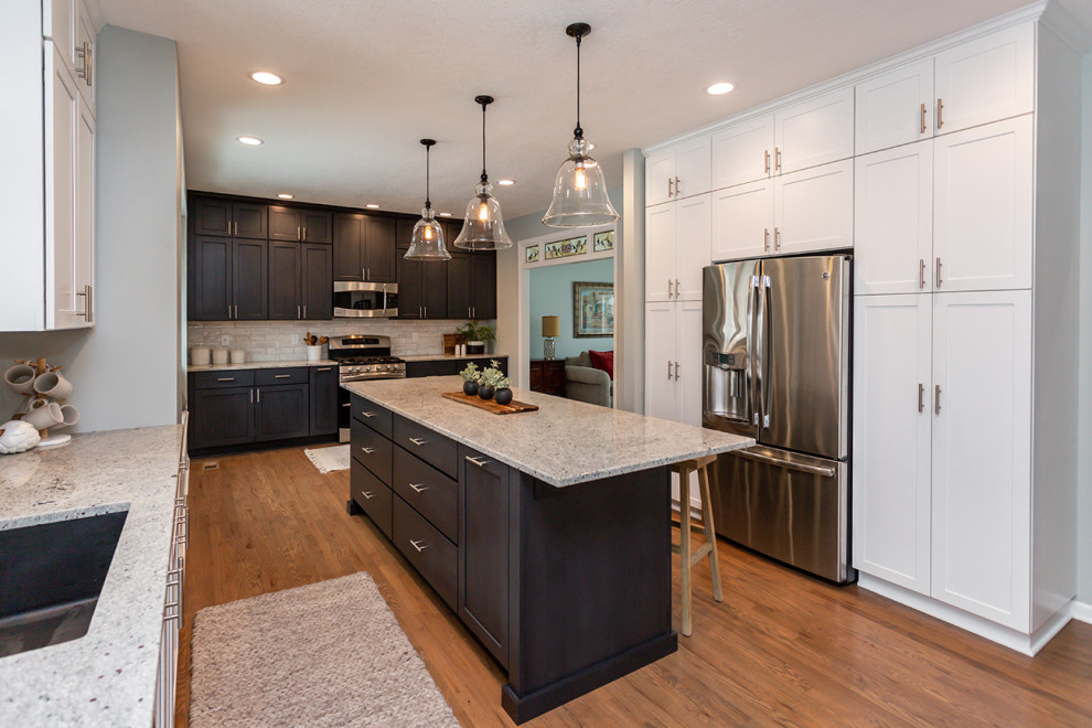 Large transitional u-shaped medium tone wood floor and brown floor eat-in kitchen photo with an undermount sink, recessed-panel cabinets, white cabinets, granite countertops, white backsplash, subway tile backsplash, stainless steel appliances, an island and gray countertops