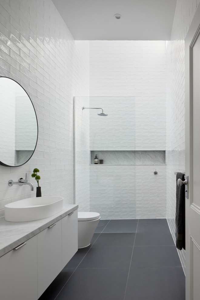 Cette image montre une grande salle de bain principale design avec des portes de placard blanches, une douche ouverte, un carrelage blanc, un carrelage métro, un plan de toilette en marbre, aucune cabine et meuble-lavabo encastré.