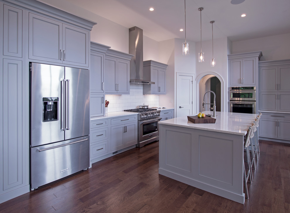 Transitional l-shaped dark wood floor and brown floor eat-in kitchen photo with an undermount sink, shaker cabinets, gray cabinets, quartz countertops, white backsplash, ceramic backsplash, stainless steel appliances, an island and white countertops