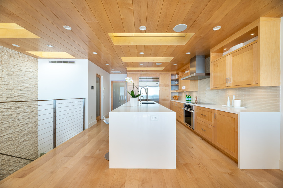 This is an example of an expansive contemporary galley open plan kitchen in Los Angeles with a single-bowl sink, shaker cabinets, light wood cabinets, quartz benchtops, beige splashback, glass tile splashback, stainless steel appliances, light hardwood floors, with island, yellow floor and white benchtop.