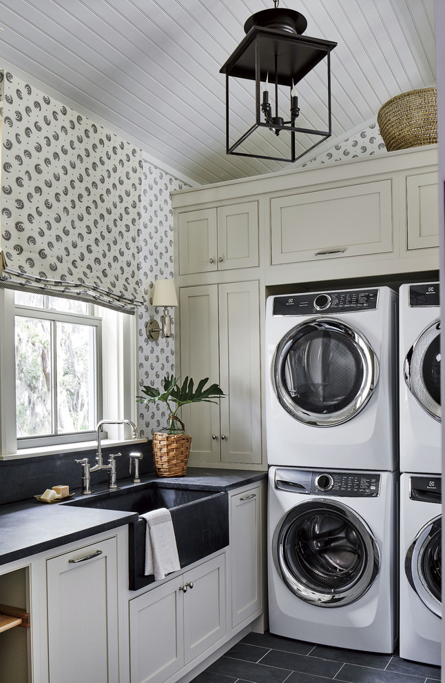 Inspiration for a beach style dedicated laundry room in Jacksonville with a farmhouse sink, shaker cabinets, grey cabinets, multi-coloured walls, black floor and black benchtop.