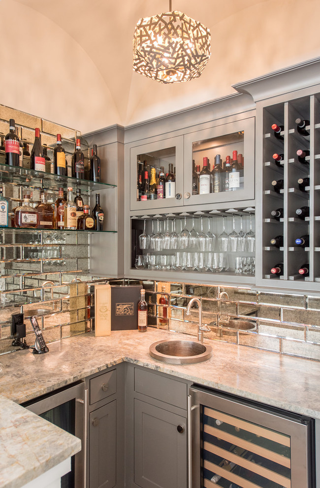 This is an example of a mid-sized beach style u-shaped wet bar in Houston with a drop-in sink, grey cabinets, granite benchtops, mirror splashback, grey benchtop and glass-front cabinets.