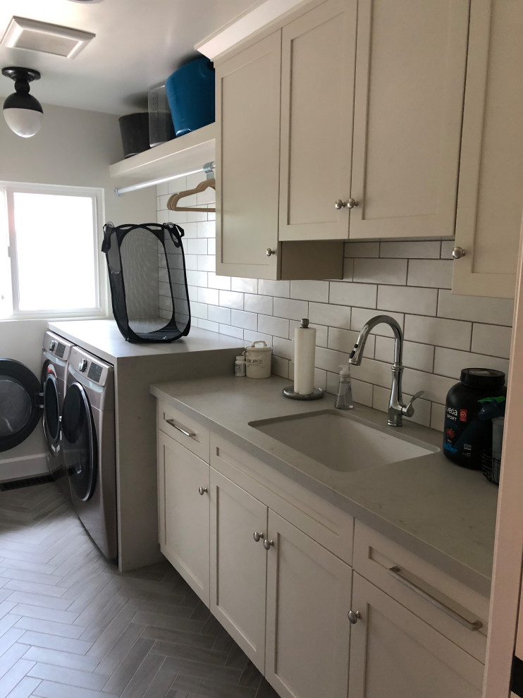 This is an example of a mid-sized traditional u-shaped dedicated laundry room in San Francisco with an undermount sink, recessed-panel cabinets, white cabinets, quartz benchtops, white splashback, subway tile splashback, beige walls, medium hardwood floors, a side-by-side washer and dryer, beige floor and grey benchtop.