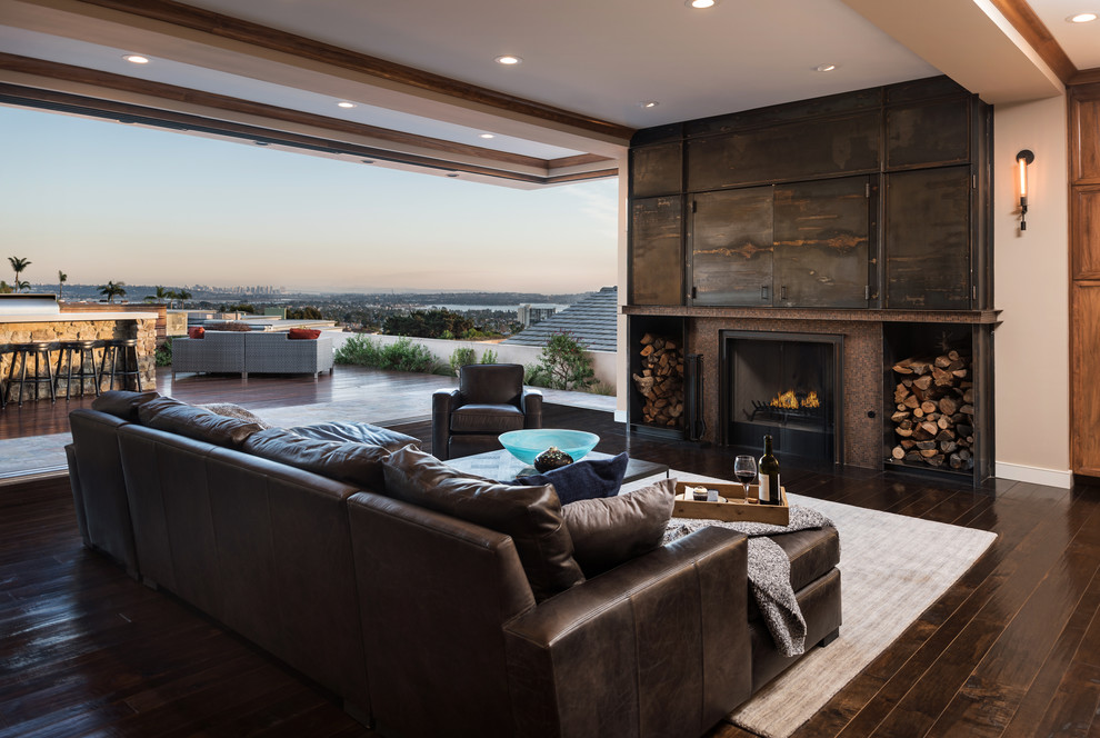 Photo of a large transitional open concept family room in San Diego with a home bar, beige walls, dark hardwood floors, a standard fireplace, a metal fireplace surround, a concealed tv and brown floor.