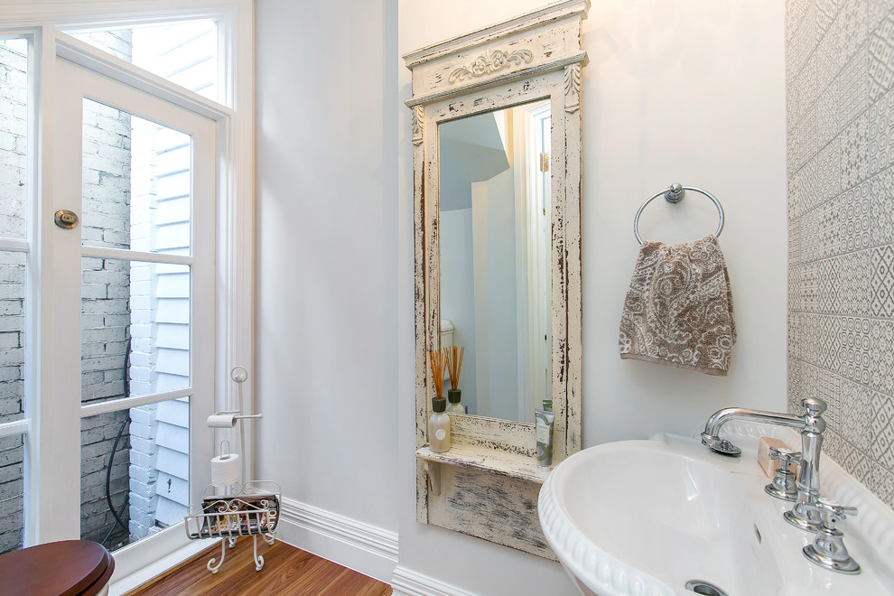 Photo of a traditional powder room in Melbourne with a pedestal sink, a two-piece toilet, porcelain tile, white walls, medium hardwood floors and gray tile.