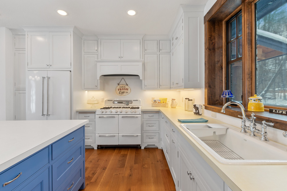 Cette image montre une cuisine américaine rustique avec des portes de placard blanches, un électroménager blanc, un sol en bois brun, îlot, un sol marron et un plan de travail blanc.