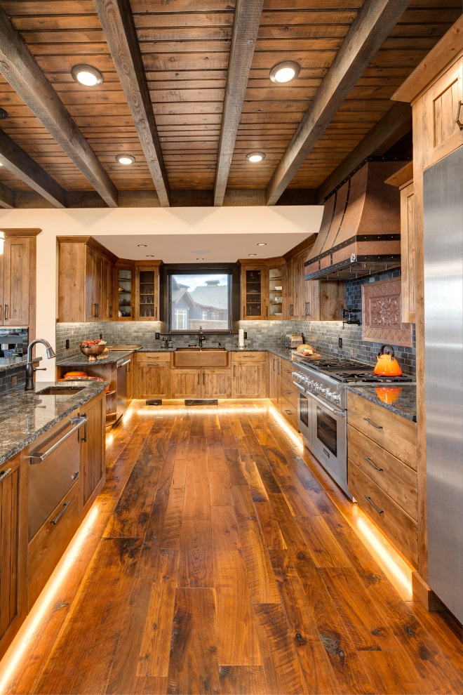 Photo of a country u-shaped kitchen in Other with a farmhouse sink, shaker cabinets, medium wood cabinets, black splashback, stainless steel appliances, medium hardwood floors, with island, brown floor, black benchtop, exposed beam, wood and quartzite benchtops.