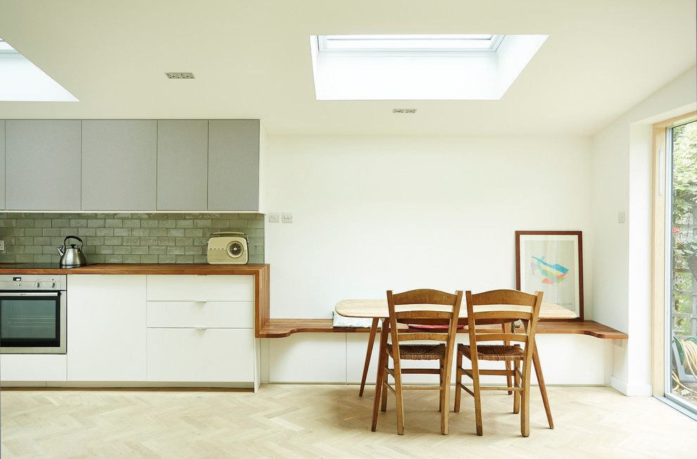 This is an example of a contemporary kitchen/dining combo in London with white walls and light hardwood floors.